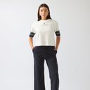 Woman wearing a white t-shirt with green and blue accents and dark pants on a white background