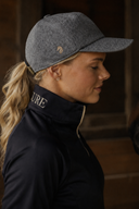 Woman wearing a dark gray cap and black jacket with 'cavvalure' branding, standing next to a horse.